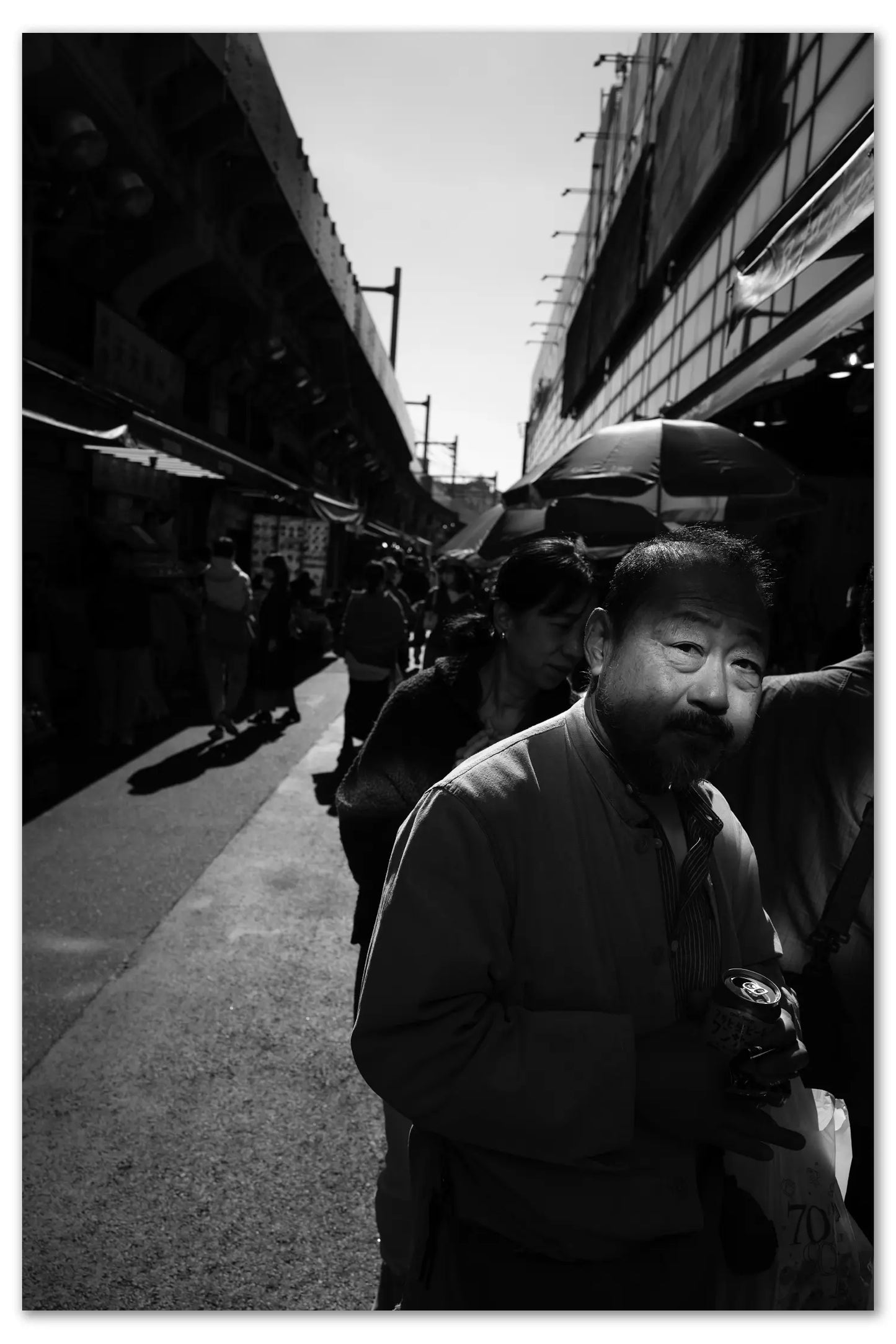 Black and white photo of a man standing on Ueno Market street with people and buildings in the background
