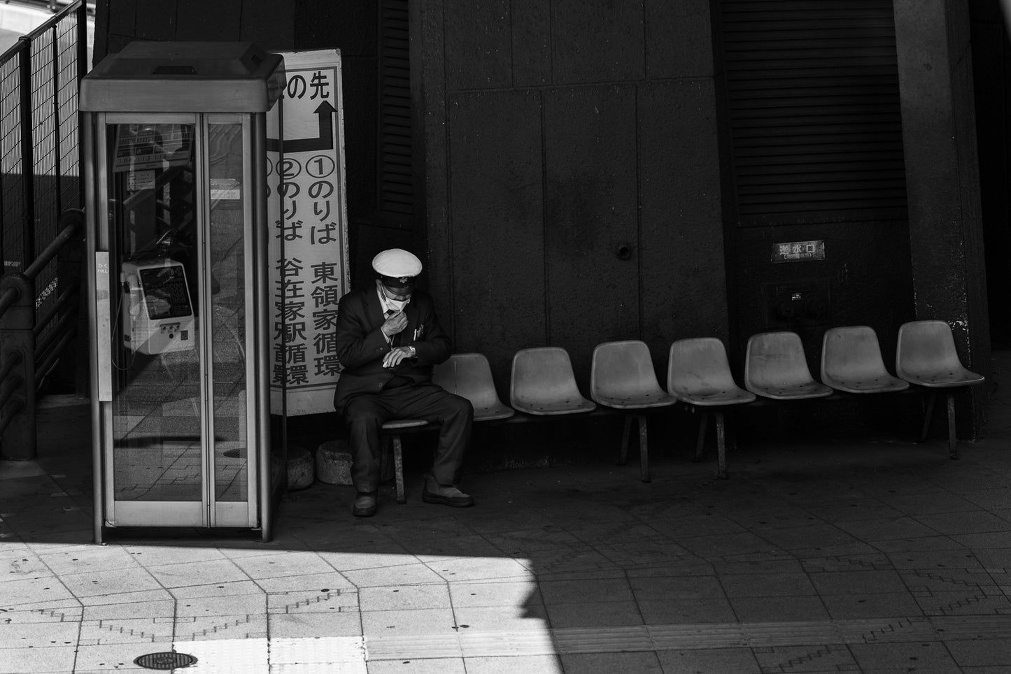 A bus driver checks his watch next to a phone booth, Kawaguchi.