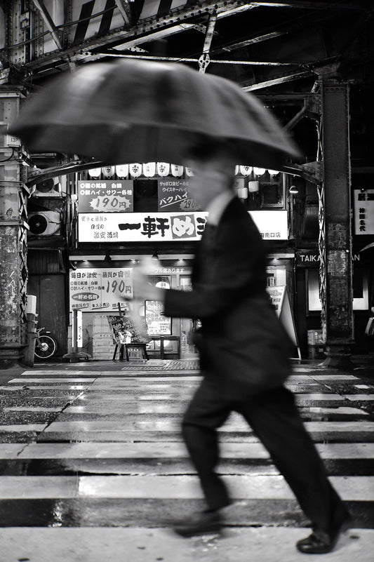 A man streaks through a Kanda crosswalk in the rain.