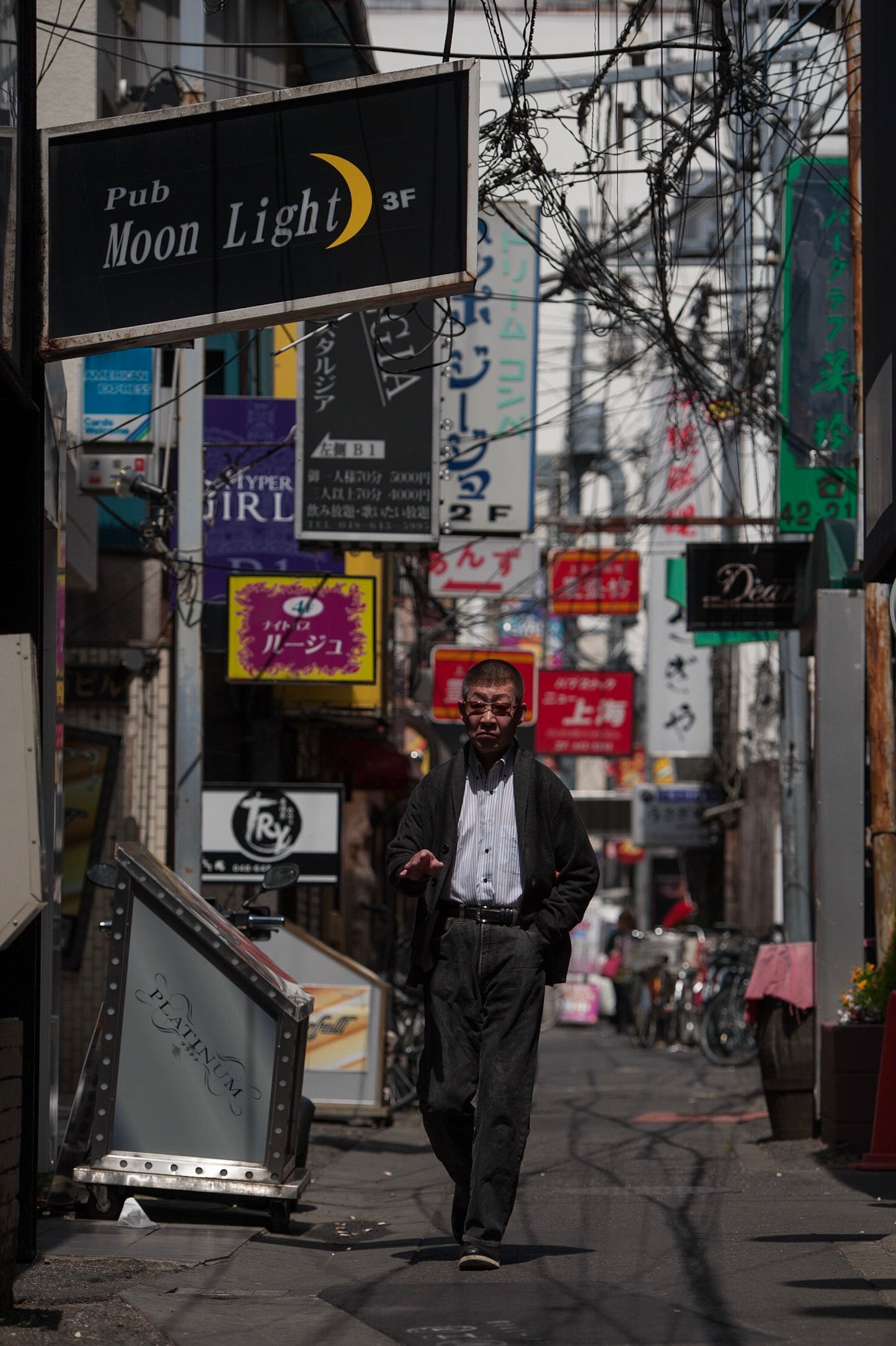 An older man walking in the bar area of Omiya in the daytime.