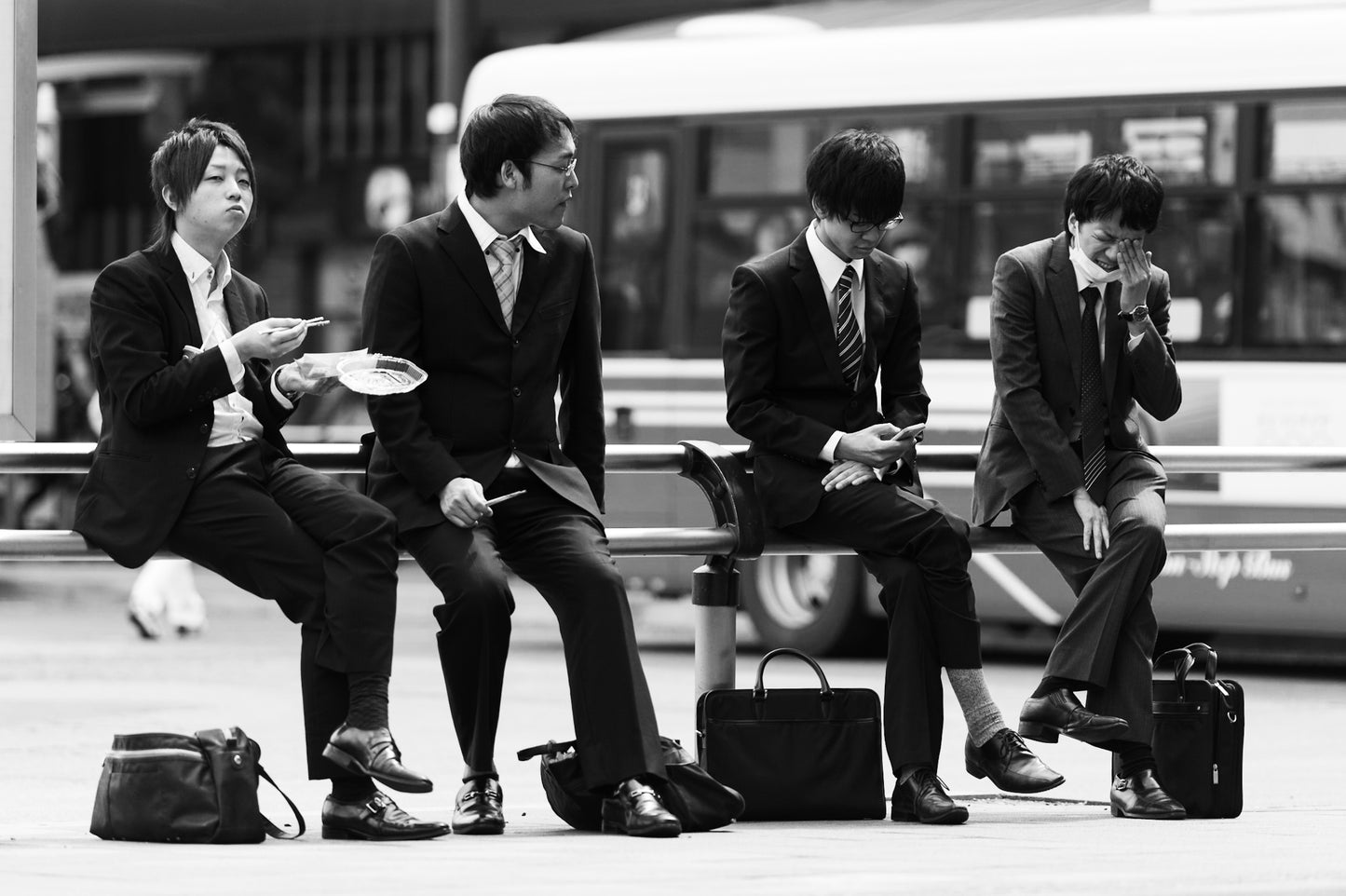 Four guys are eating lunch at the Omiya station bus stop.