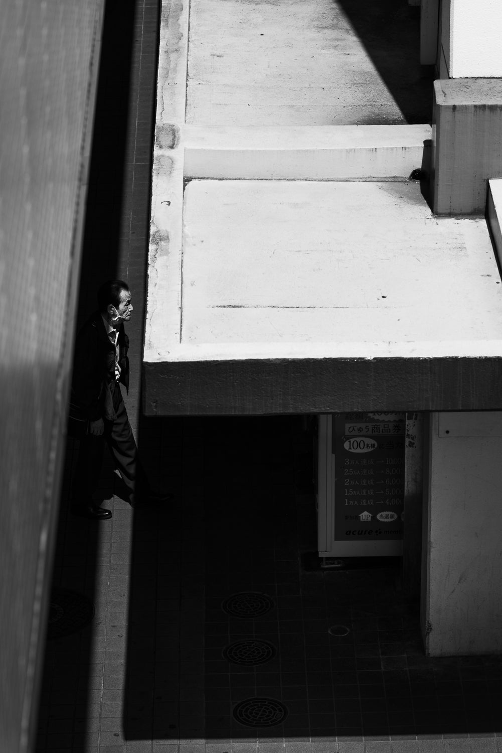 A man walks in a crack of light between buildings, Kawaguchi.