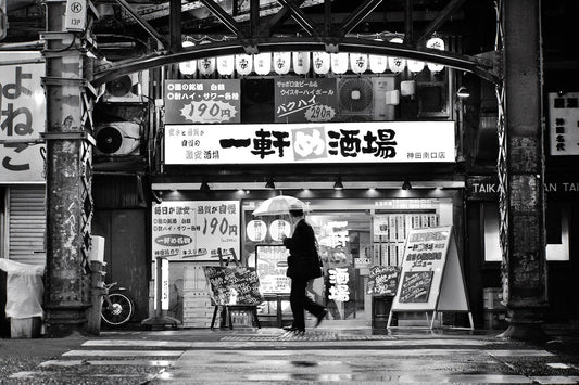 A man with an umbrella walks past a restaurant at in the rain at Kanda Station, Tokyo.