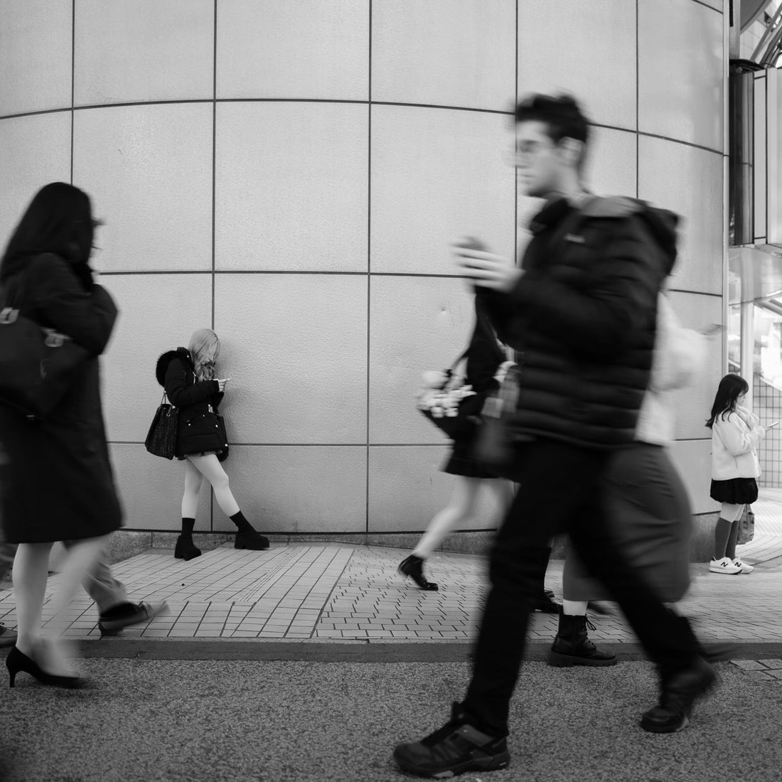 A woamn looks at her phone as people walk past in a blur, Shibuya 109.