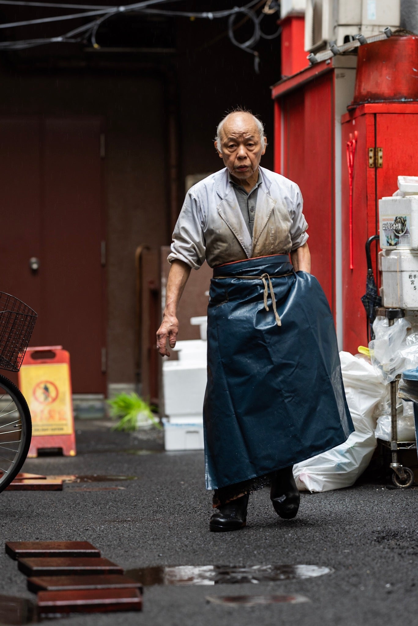 A fishmonger walks behind a shop in the rain.