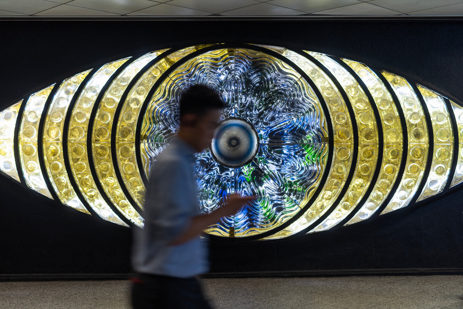 An out of focus man looking at his smartphone walks past the Shinjuku eye.