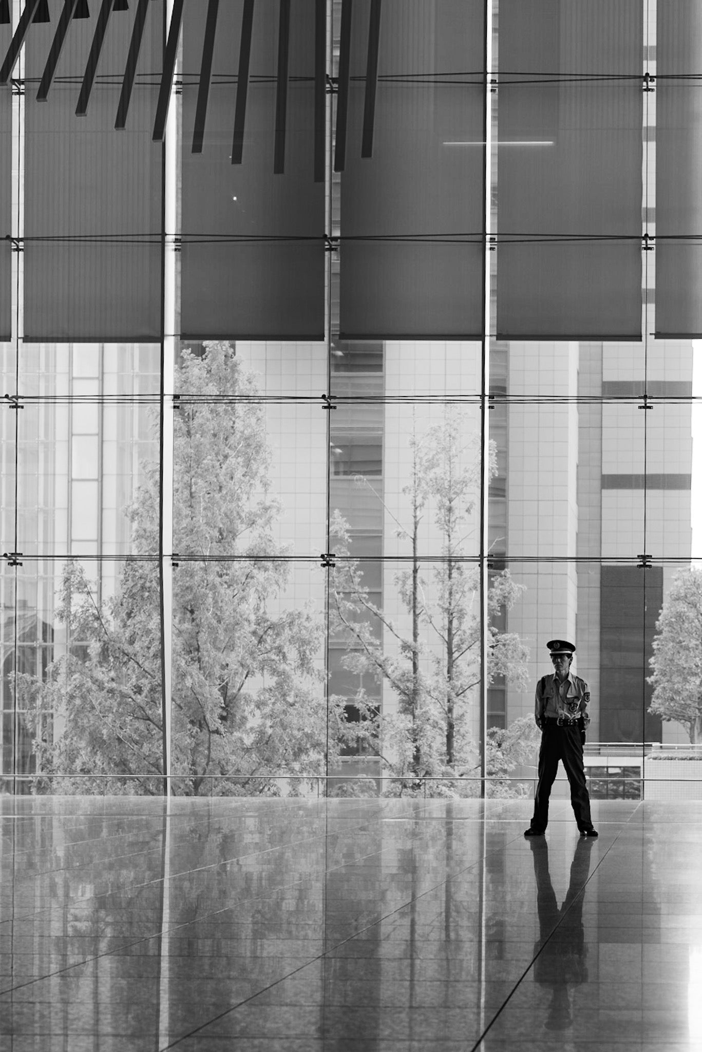 A lack and white image of a security guard and his reflection in an office building lobby.